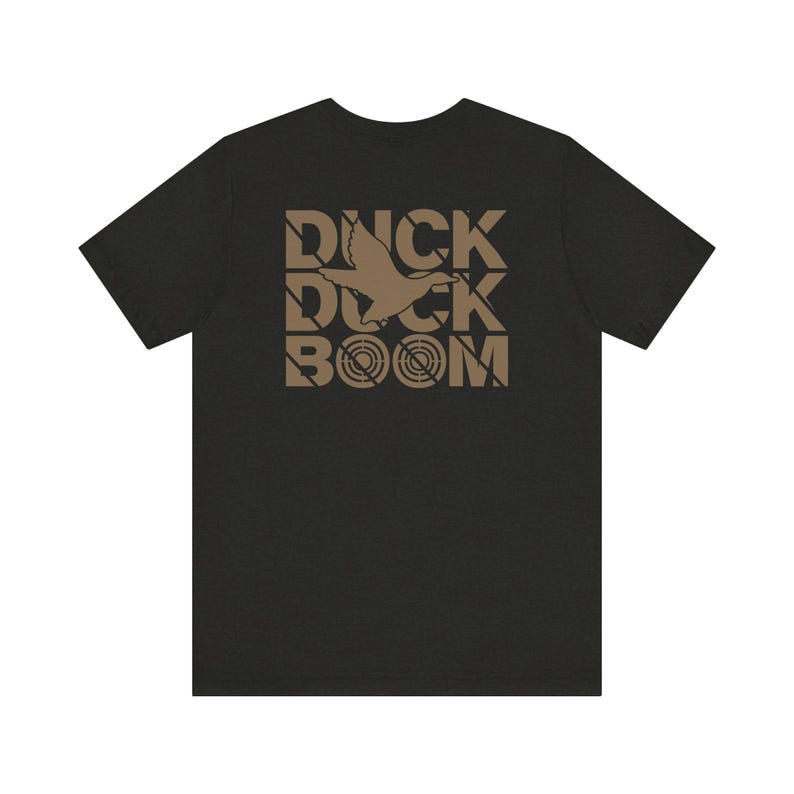 Puede incluir: Una camiseta gris oscuro con un estampado gr&aacute;fico marr&oacute;n de un pato volando con el texto "DUCK BOOM" impreso en la espalda.
