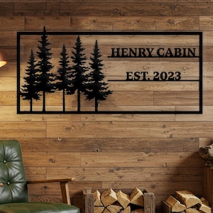 Könnte beinhalten: Schwarze Wandkunst aus Metall mit einer Silhouette von Kiefern mit dem Text "HENRY CABIN EST. 2023" im rustikalen Kabinenstil.