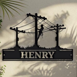 May include: Black metal silhouette of a lineman working on power lines with the name "HENRY" on a black rectangular plaque.
