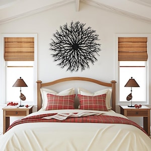 May include: A bedroom with a white wall and a black metal wall sculpture in the shape of a tree branch. The bed has a white duvet, red and white plaid pillows, and a red and white striped throw blanket. There are two nightstands with lamps on either side of the bed.
