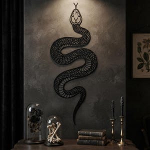 Op de afbeelding: Een zwarte, aan de muur gemonteerde slangensculptuur met een gedetailleerd, ingewikkeld rasterpatroon over het hele lichaam. De slang is afgebeeld in een kronkelende S-vorm met de kop aan de bovenkant, voorzien van een gestileerd ontwerp.