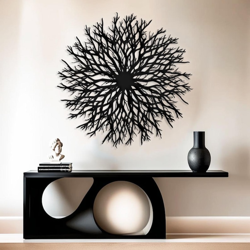 May include: Black metal wall art in the shape of a large, circular, branching tree. The art is hanging on a white wall above a black console table with a white round object in the center.