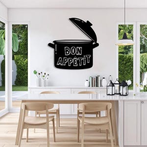 May include: Black metal wall art in the shape of a cooking pot with the lid open. The words "BON APPETIT" are displayed in white lettering on the pot. The art is mounted on a white wall in a kitchen setting.