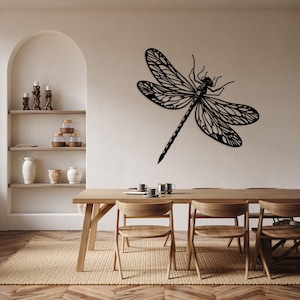 May include: A black metal dragonfly wall decor with intricate details hangs above a wooden dining table with chairs. The table is set with cups and saucers.