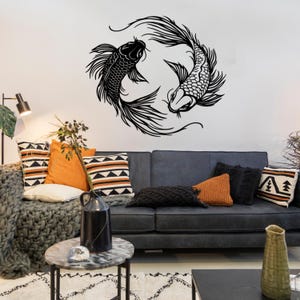 Puede incluir: Pegatina de pared de silueta en blanco y negro de dos peces koi nadando en c&iacute;rculo. La pegatina est&aacute; en una pared blanca sobre un sof&aacute; gris con almohadas.
