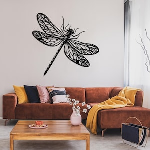 May include: A black metal dragonfly wall decor with intricate details, mounted on a white wall above a brown sectional sofa with yellow and brown throw pillows.