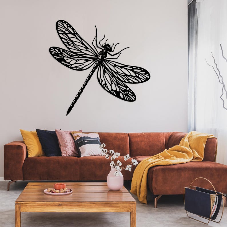 May include: A black metal dragonfly wall decor with intricate details, mounted on a white wall above a brown sectional sofa with yellow and brown throw pillows.