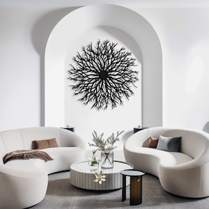 May include: A black metal wall sculpture in the shape of a large, circular, branching tree. The sculpture is hanging on a white wall in a modern living room with two white curved sofas and a coffee table.