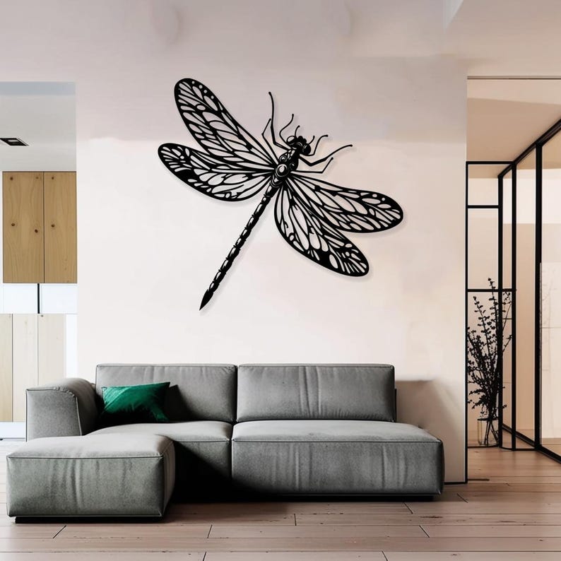 May include: Black metal dragonfly wall decor with intricate wing details. The dragonfly is mounted on a white wall above a gray sectional sofa.