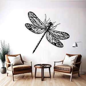 May include: Black metal dragonfly wall decor with intricate details, hanging on a white wall above two brown armchairs and a wooden coffee table.