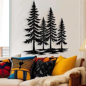 Könnte beinhalten: Schwarze Metall-Wandkunst mit vier stilisierten Kiefern. Die Bäume sind an einer weißen Wand über einem Sofa mit bunten Zierkissen angebracht. Die Kissen haben verschiedene Muster und Farben, darunter Gelb, Blau und Rot.