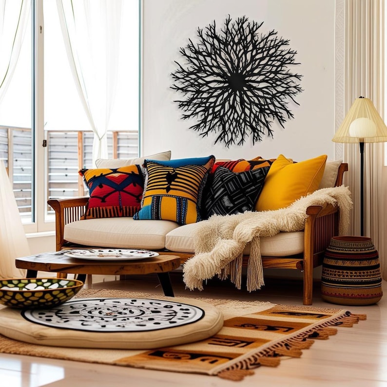 May include: A white couch with colorful patterned throw pillows and a fluffy white blanket. A black metal wall sculpture resembling a tree branch is hanging on the wall behind the couch. A wooden coffee table with a plate on it sits in front of the couch. A round, patterned cushion sits on the floor in front of the couch.