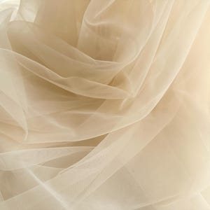 May include: A sheer, light beige tulle fabric with a soft, flowing texture.