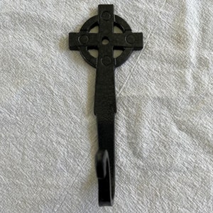 May include: Black metal Celtic cross hook. The hook is shaped like a Celtic cross with a rounded top and a single hook at the bottom.