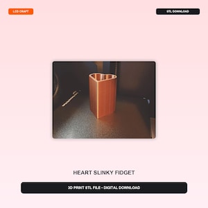 May include: A copper-colored 3D printed heart-shaped container with a ribbed, textured surface. The object features a hollow center and a distinct heart-shaped rim. The text LCD CRAFT, STL DOWNLOAD, HEART SLINKY FIDGET, and 3D PRINT STL FILE • DIGITAL DOWNLOAD are visible.