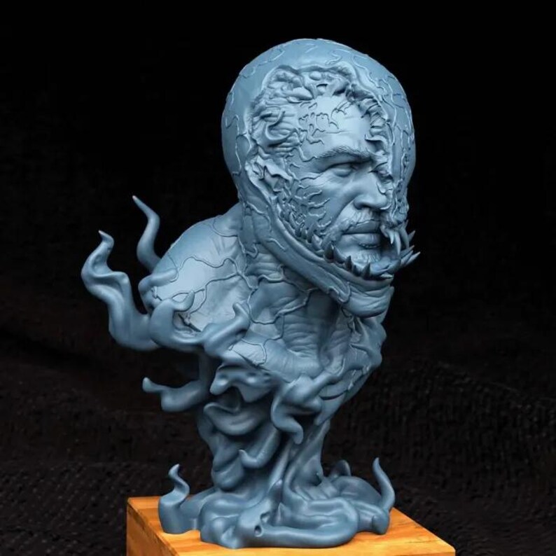 以下が含まれることがあります： 青い3Dプリントされた、モンスターのような質感のある顔と、流れるような有機的な土台を持つキャラクターの胸像