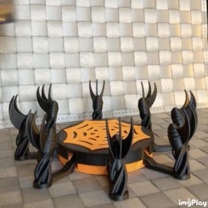 以下が含まれることがあります： 黒とオレンジ色のハロウィーンをテーマにしたテーブル。6つの様式化された湾曲した脚があります。テーブルは、クモの巣のデザインと黒いベースを備えた丸い天板を持っています。脚はねじれており、湾曲しています。