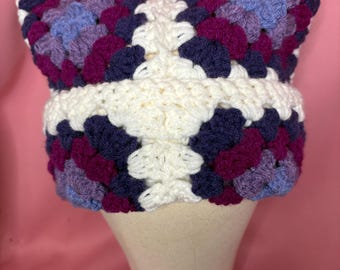 May include: A white crocheted hat with a granny square pattern in shades of purple, blue, and white.