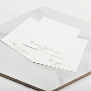 Pu&ograve; includere: Tre carte bianche con messaggi diversi scritti in corsivo. I messaggi sono "Buon Natale", "Mamma" e "Grazie".