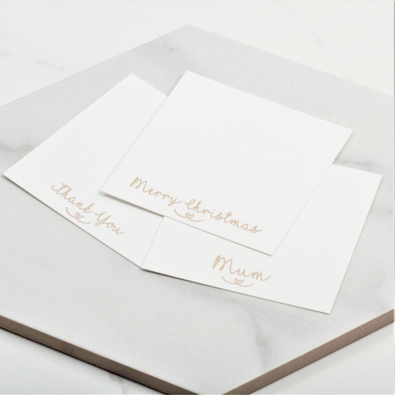 Pu&ograve; includere: Tre carte bianche con messaggi diversi scritti in corsivo. I messaggi sono "Buon Natale", "Mamma" e "Grazie".