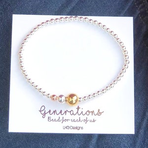 May include: A silver beaded bracelet with a gold bead and the text "Generations Bead for each of us LHO Designs".