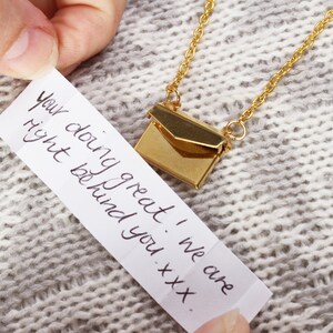 May include: A gold necklace with a small envelope charm. The envelope opens to reveal a handwritten note that reads "You're doing great! We care right behind you - xxx."
