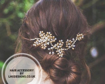 May include: A gold hair accessory with pearl and crystal accents. The accessory is in the shape of a vine with leaves and flowers. The accessory is worn in a woman's hair.