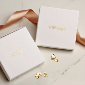 May include: Two white square boxes with the text "LHO Designs" printed in gold on the top of each box. The boxes are on a white marble surface with gold foil confetti.