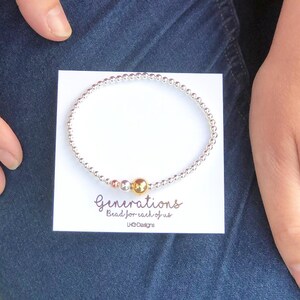 May include: A silver and gold beaded bracelet with the text "Generations Bead for each of us LHO Designs".