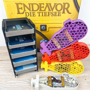 Könnte beinhalten: Brettspiel "Endeavor Die Tiefsee" mit verschiedenen Komponenten. Enthält einen schwarzen Kartenhalter mit blauen Karten und farbige U-Boot-förmige Teile in Lila, Rot und Gelb. Außerdem ein weißes U-Boot-förmiges Tablett.