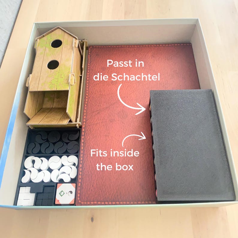 May include: A brown cardboard box with a red felt insert and black foam inserts. The box contains a wooden birdhouse, black and white game pieces, and a small game board. The text "Fits inside the box" and "Passt in die Schachtel" is written on the felt insert.