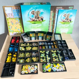 Könnte beinhalten: Ein Brettspiel namens "Arche Nova" mit einer blauen und grünen Schachtel, einem Spielbrett und verschiedenen Spielsteinen. Die Spielsteine sind in schwarzen Plastikbehältern organisiert.