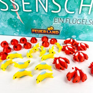 Könnte beinhalten: Ein Brettspiel mit verschiedenen Spielsteinen. Die Spielsteine umfassen rote, gelbe und weiße Kunststoffkomponenten. Die Spielbox ist türkis mit weißem Text und dem Feuerland-Logo. Die Spielsteine sind auf einer weißen Oberfläche angeordnet.