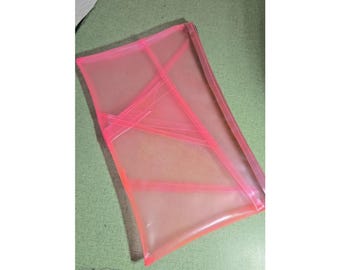 May include: A rectangular, semi-transparent neon pink pouch made of a flexible plastic material. The pouch features a series of diagonal, overlapping structural seams or reinforced lines across its surface, creating a geometric pattern.