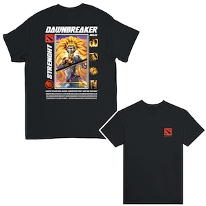 Puede incluir: Camisetas negras con un gráfico de un personaje con cabello rubio y el texto "DAWNBREAKER" y "STRENGHT". La parte posterior de la camiseta tiene el logotipo de Dota 2 en rojo. La parte delantera de la camiseta tiene el texto "LEAPS TO AID HER ALLIES, WHEREVER THEY ARE ON THE MAP".