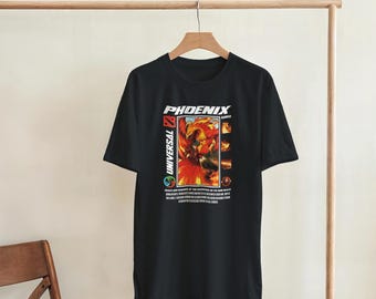Puede incluir: Una camiseta negra de manga corta con un estampado gráfico en el pecho. El diseño incluye el texto PHOENIX y UNIVERSAL, una ilustración central de un pájaro de fuego naranja y rojo, y paneles rectangulares más pequeños con texto.