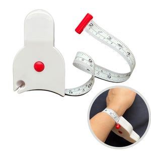 Pode incluir: Uma fita métrica de pulso de plástico branco com um botão vermelho e uma ponta vermelha. A fita é marcada em centímetros e é enrolada em volta de um pulso em uma inserção circular.