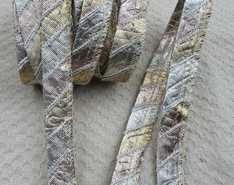 Könnte beinhalten: Eine Rolle dekoratives Band mit einem sich wiederholenden diagonalen Muster aus metallisch goldenen, silbernen und kupferfarbenen Abschnitten. Das Band hat eine strukturierte, gewebte Optik mit ausgefransten Kanten und einem deutlichen Glanz.