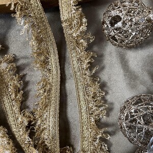 May include: Two strands of gold fringe trim with a shimmery finish. The trim has a delicate, frayed edge.