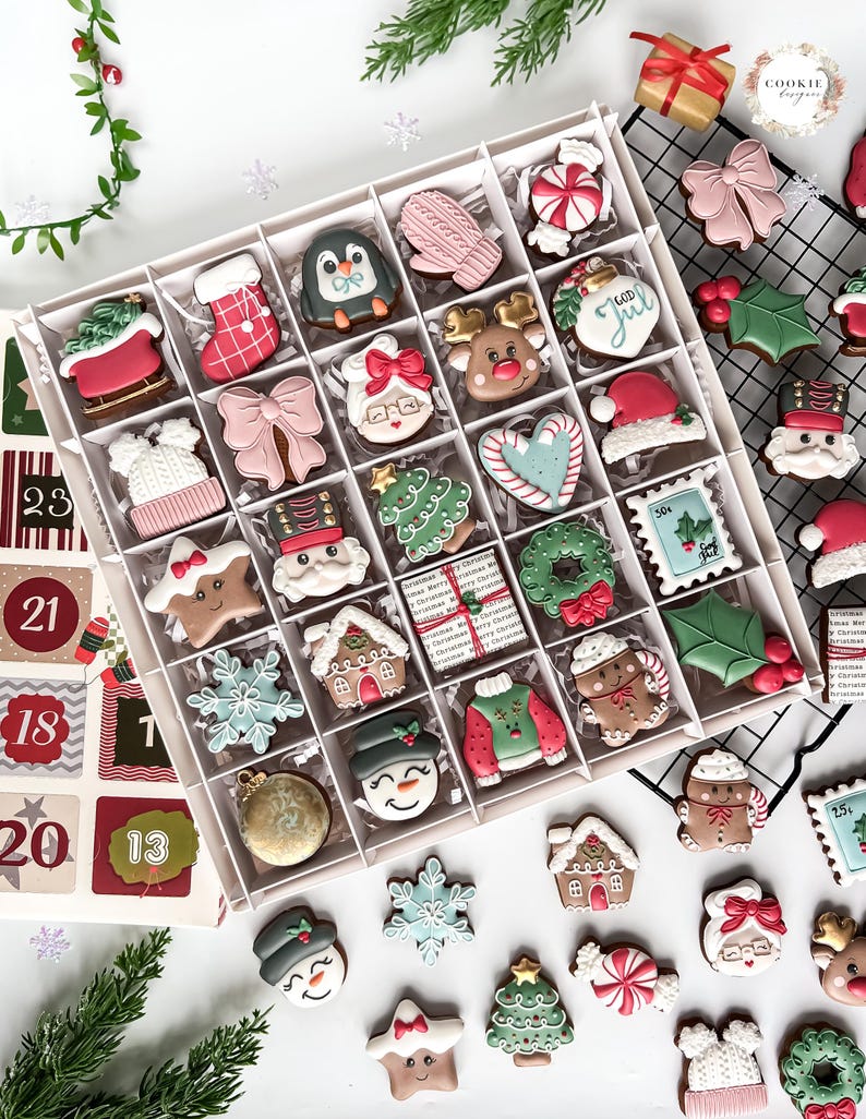K&ouml;nnte beinhalten: Eine Box mit weihnachtlichen Keksen, die jeweils mit festlichen Designs verziert sind. Die Kekse umfassen Lebkuchenh&auml;user, Schneem&auml;nner, Weihnachtsb&auml;ume und Rentiere in verschiedenen Farben. Ein Adventskalender ist ebenfalls zu sehen.