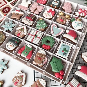 K&ouml;nnte beinhalten: Eine Schachtel mit dekorierten Weihnachtspl&auml;tzchen, darunter Lebkuchenm&auml;nner, Weihnachtsm&uuml;tzen und Schneeflocken. Die Kekse sind in verschiedenen Formen und Farben gehalten und weisen aufwendige Verzierungen auf. Einige Kekse tragen den Text "GOD JUL".
