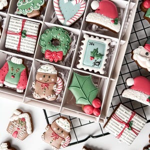 K&ouml;nnte beinhalten: Eine Schachtel mit dekorierten Weihnachtspl&auml;tzchen. Die Kekse haben verschiedene Formen, darunter ein Weihnachtsbaum, ein Herz mit Zuckerstangenstreifen, eine Weihnachtsm&uuml;tze, ein Kranz, ein Pullover, ein Lebkuchenmann und eine Geschenkbox.