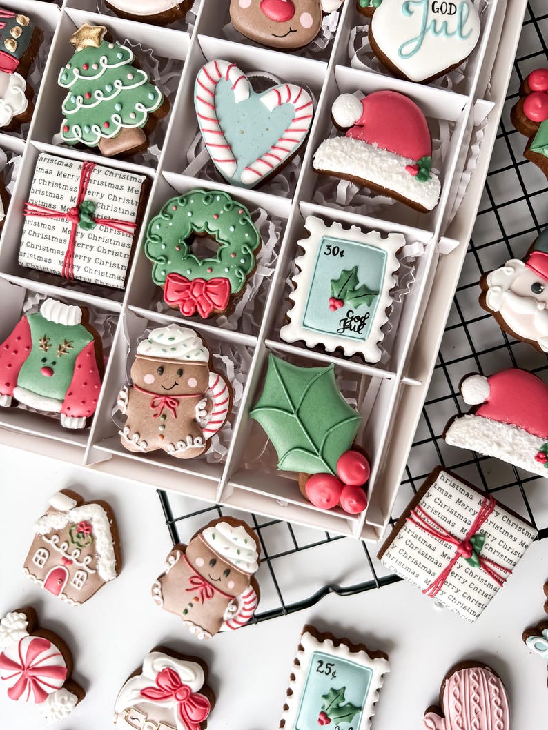 K&ouml;nnte beinhalten: Eine Schachtel mit dekorierten Weihnachtspl&auml;tzchen. Die Kekse haben verschiedene Formen, darunter ein Weihnachtsbaum, ein Herz mit Zuckerstangenstreifen, eine Weihnachtsm&uuml;tze, ein Kranz, ein Pullover, ein Lebkuchenmann und eine Geschenkbox.