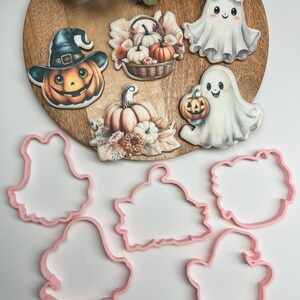 K&ouml;nnte beinhalten: Satz mit sechs Halloween-Ausstechern, darunter ein Geist, ein K&uuml;rbis, ein Hexenhut und drei verschiedene Herbstmotive. Die Ausstecher sind rosa und aus Kunststoff.