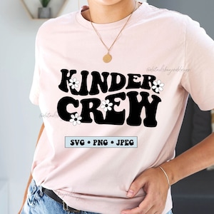 Può includere: Una maglietta rosa con il testo "Kinder Crew" in lettere nere in stile retrò con fiori bianchi. Il testo "SVG PNG JPEG" è sotto il testo principale.