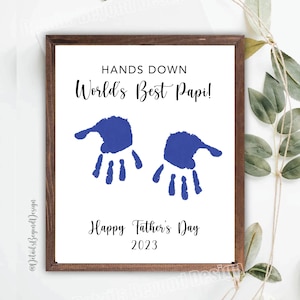 May include: A white framed print with blue handprints and the text "HANDS DOWN World's Best Papi! Happy Father's Day 2023".