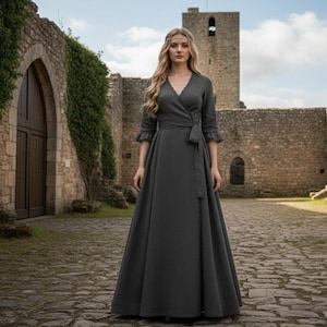 Può includere: Un abito a portafoglio grigio scuro con scollo a V, maniche a tre quarti e cintura abbinata. L'abito ha una gonna lunga e fluida. La scena è ambientata di fronte a un castello di pietra.