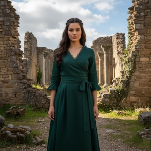 Puede incluir: Un vestido cruzado verde oscuro con escote en V y lazo en la cintura. El vestido tiene mangas tres cuartos con puños con volantes. El fondo presenta ruinas de piedra y un cielo nublado.