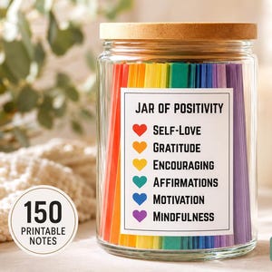 May include: A clear glass jar with a wooden lid filled with rainbow-colored paper strips. A white label on the front reads JAR OF POSITIVITY with six colored hearts next to the words Self-Love, Gratitude, Encouraging, Affirmations, Motivation, Mindfulness.