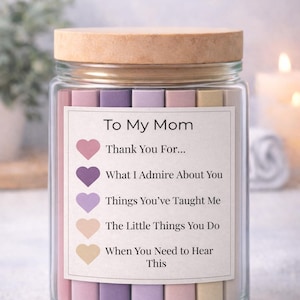 Pode incluir: Um frasco de vidro com tampa de madeira, preenchido com tiras de papel coloridas. Um rótulo diz "To My Mom" com indicações como "Thank You For..." e "What I Admire About You". O frasco é um presente atencioso.